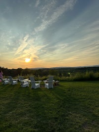 a group of white lawn chairs on a grassy field at sunset