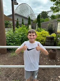 a boy giving a thumbs up in front of a roller coaster